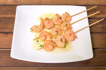 Garlic prawn skewer with olive oil on white plate on wooden table