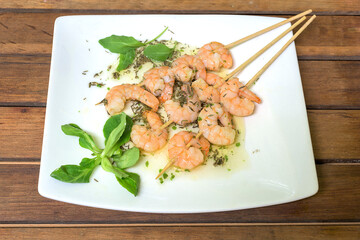Garlic prawn skewer with olive oil on a white plate with lettuce leaves and lamb's lettuce