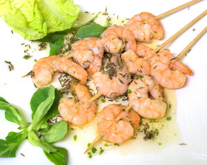 Garlic prawn skewer with olive oil on a white plate with lettuce leaves and lamb's lettuce
