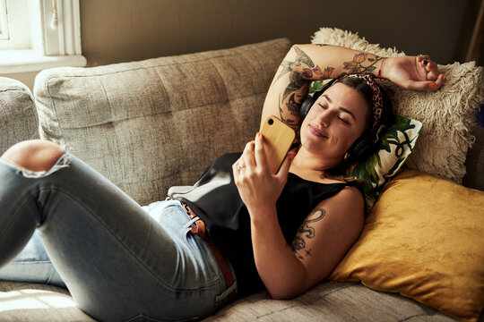 Home, relax and woman on sofa, smartphone and internet with social media, texting and communication. Headphones, person or girl on couch, cellphone or typing with message to contact or calm in lounge