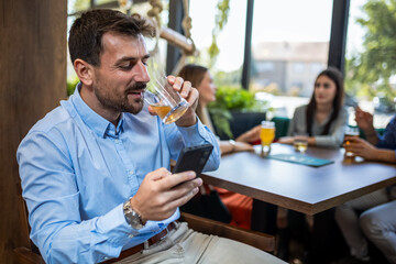 Businessman using his phone in the restaurant. Smiling and drinking beer.