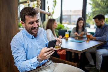 Businessman using his phone in the restaurant. Smiling and drinking beer.
