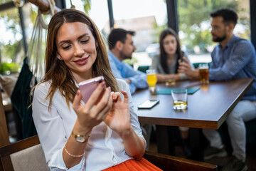 Woman using her phone in the restaurant. Her friends are in the background.