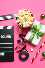 Movie clapper with popcorn, film reel and Christmas decor on pink background