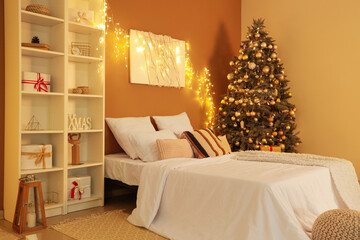 Interior of bedroom with glowing lights, painting and Christmas tree in evening