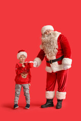 Santa Claus and cute little boy with cups of hot chocolate on red background