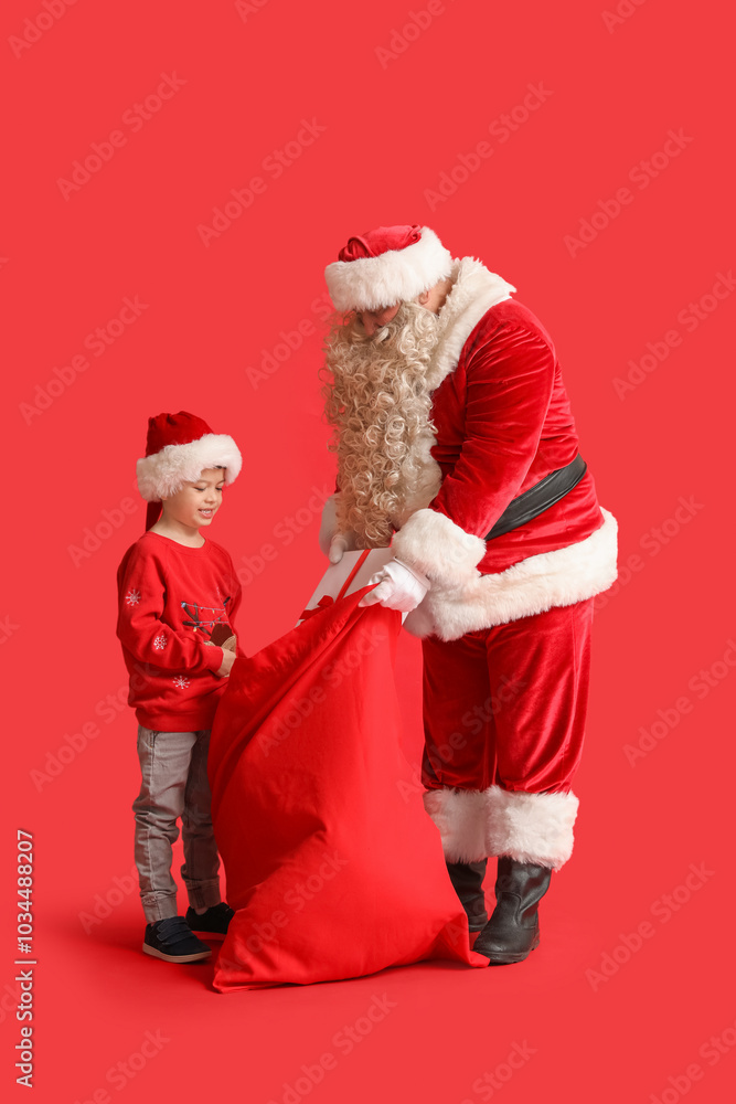 Poster Santa Claus and cute little boy with bag full of Christmas gifts on red background