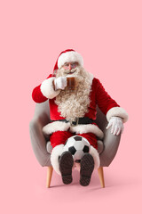 Santa Claus with mug of beer and soccer ball in armchair on pink background