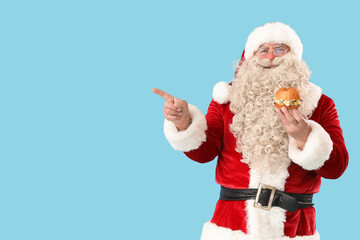 Santa Claus with tasty burger pointing at something on blue background