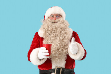 Santa Claus with cup of tea showing thumb-up on blue background