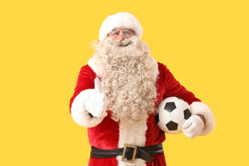 Santa Claus with soccer ball showing thumb-up on yellow background