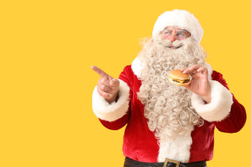 Santa Claus with tasty burger pointing at something on yellow background