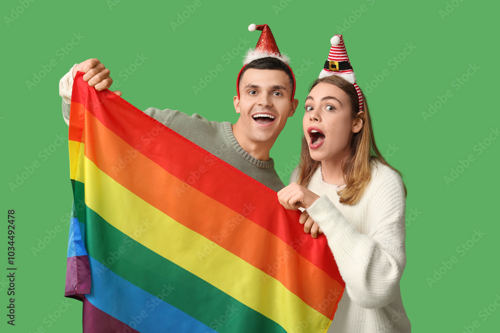 Canvas Prints Young couple in Santa hats with LGBT flag on green background