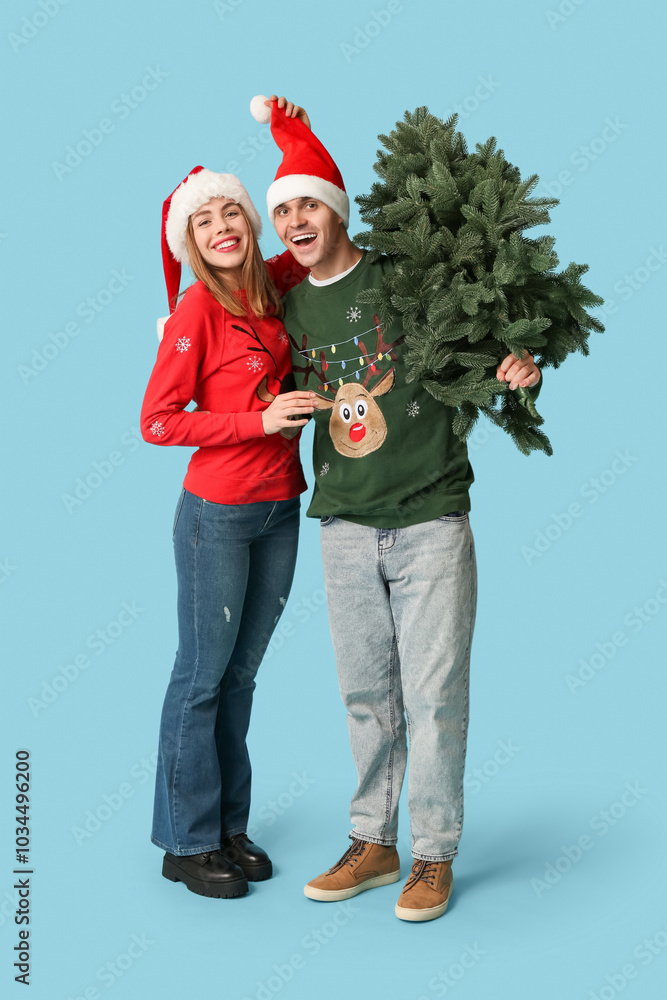 Poster Happy young couple in Santa hats with Christmas tree on blue background