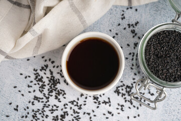 Cup of oil and jar with sesame seeds on white grunge background