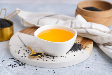 Bowl of oil with spoon and sesame seeds on white grunge background