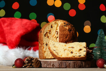 Wooden board with cut Panettone and Christmas decor on dark blurred background