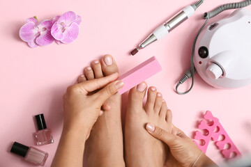Young woman with beautiful pedicure using nail buffer on pink background