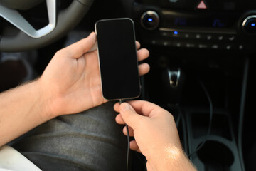 Male driver connecting charging cable to mobile phone in car, closeup