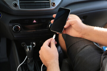 Man connecting white charging cable to mobile phone in car, closeup