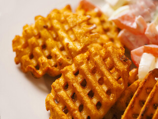Cooked potato chips fries in a lattice shape on a white plate. Selective focus. Marketing move to...