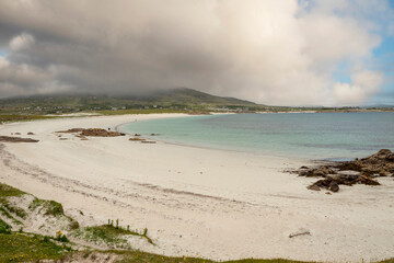 White sandy beach and ocean with blue turquoise color water. Dog bay, county Galway, Ireland. Popular tourist area with stunning Irish nature scenery. Cloudy sky. Travel and tourism.