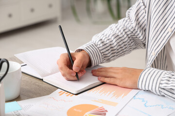 Male economist writing on notebook at table in office, closeup