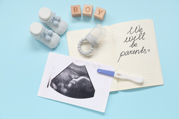 Baby shoes, sonogram image, pregnancy test and notebook with text WE WILL BE PARENTS on blue...
