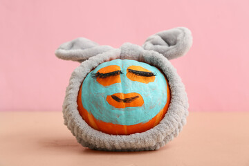 Funny pumpkin with false eyelashes, cosmetic mask and headband on color background