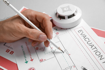 Man with smoke detector drawing evacuation plan on grey background, closeup © Pixel-Shot