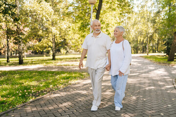 Full length portrait of senior couple enjoying leisurely stroll in green park, holding hands...