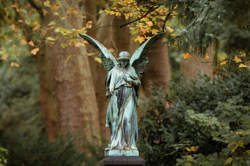 an angel with wings in front of autumn leaves in the fairytale-like, enchanted and historic Melaten...