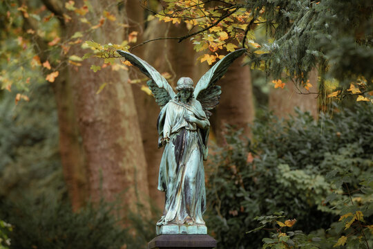 an angel with wings in front of autumn leaves in the fairytale-like, enchanted and historic Melaten Cemetery in Cologne