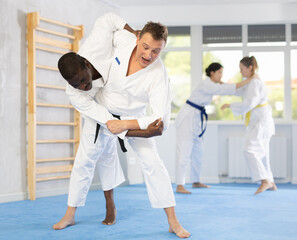 Two males practicing judo together on sports mats under the guidance of a trainer