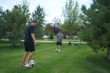 Fototapeta premium Two men are engaged in a friendly soccer match, skillfully passing the ball back and forth on a well-maintained grassy field surrounded by trees