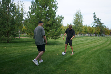 Obraz premium Two friends are playing soccer on a lush green lawn in a park, practicing their skills while enjoying the warm sunshine and fresh air. The atmosphere is relaxed and fun