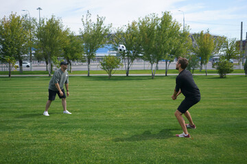 Obraz premium Two young adults engage in a lively game of volleyball outdoors in a sunny park, with vibrant greenery and a clear blue sky enhancing the cheerful atmosphere