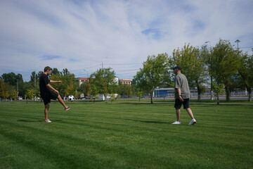 Obraz premium Two men are outdoors in a park, practicing their soccer juggling skills. One man performs ball tricks while the other watches, enjoying the sunny day among the trees