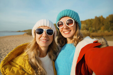 Happy young two women friends taking selfie with phone on beach, smiling girlfriends having fun