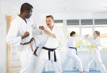 Fototapeta premium Two adult men in kimonos train judo techniques in group in studio
