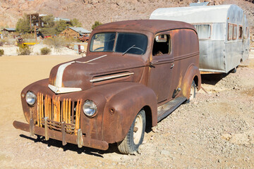 Abandoned vintage rusted vehicle with camper trailer in a desert junkyard
