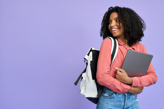 Happy young African American girl holding laptop standing isolated on purple background, smiling female student model with backpack and computer looking away advertising educational program abroad.