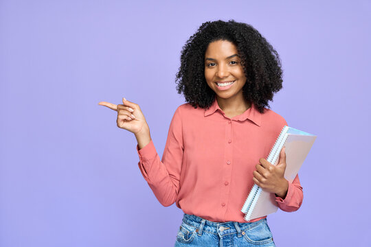 Happy young African college student model holding copybooks isolated on purple background. Smiling Afro American girl looking at camera pointing aside advertising education abroad.