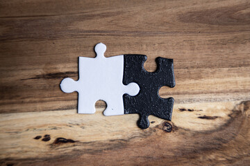 Two puzzle pieces with one black and one white on a wooden table. As a concept of unity between opposites.