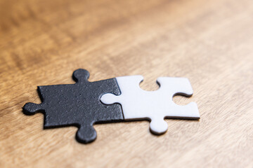 Two puzzle pieces with one black and one white on a wooden table. As a concept of unity between opposites.