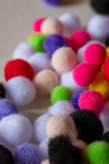 A pile of colorful pom poms are scattered on a table. The pom poms are of various sizes and colors, including red, green, yellow, and purple. Concept of playfulness and creativity