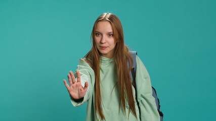 Assertive young woman doing stop hand gesture and talking. Annoyed girl doing firm halt sign gesturing, wishing to end concept, isolated over blue studio background, camera A