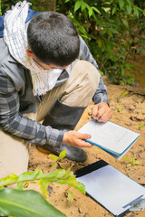 A male biologist takes notes in his notebooks while conducting research in the Amazon rainforest of Colombia.