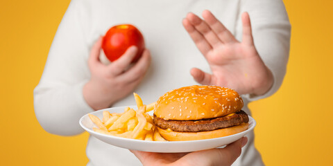 Unrecognizable plus size girl refusing to eat fast junk food, showing stop gesture with hand and...