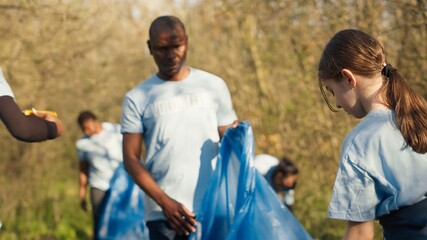 Diverse volunteers collecting garbage and junk from the forest area, fighting environmental pollution and conservation. Group of activists cleaning up the woods, recycling plastic waste. Camera A.